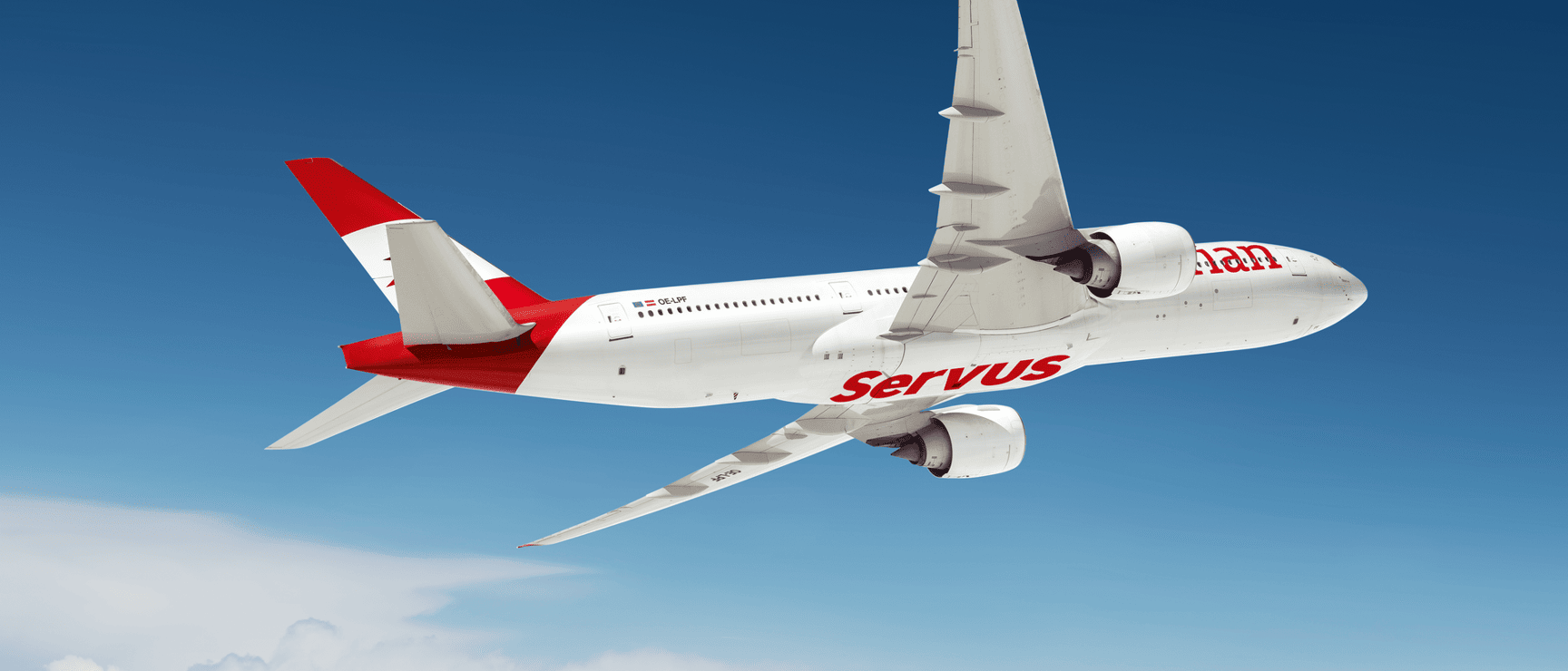 White passenger aircraft with red "Servus" lettering flying over clouds against blue sky