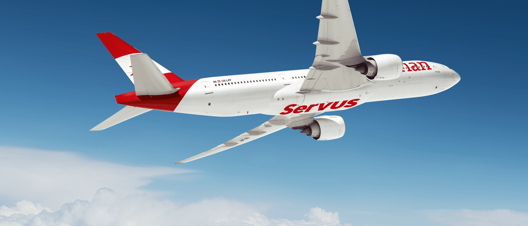 Weißes Passagierflugzeug mit rotem „Servus"-Schriftzug fliegt über Wolken vor blauem Himmel.