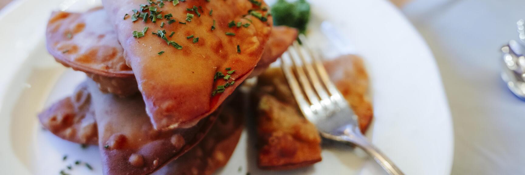 Fried pastry pockets with chives on white plate, fork beside.