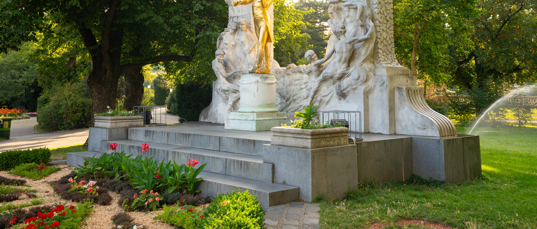 Golden Johann Strauss statue in Vienna's City Park with white marble arch and flowerbeds in foreground.