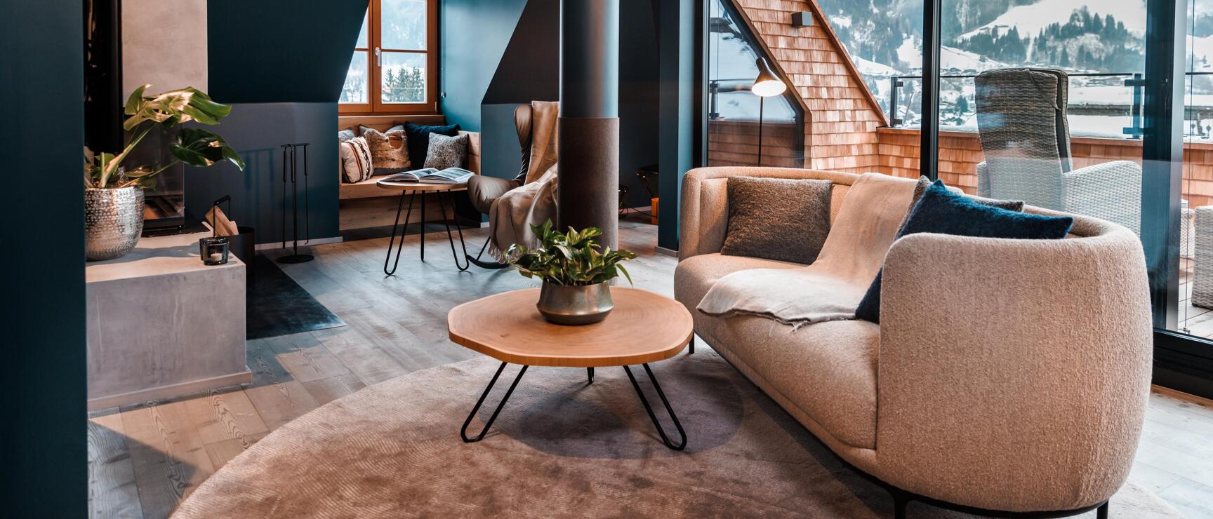 Modern hotel room with armchair, fireplace and panoramic window overlooking snow-covered mountains.