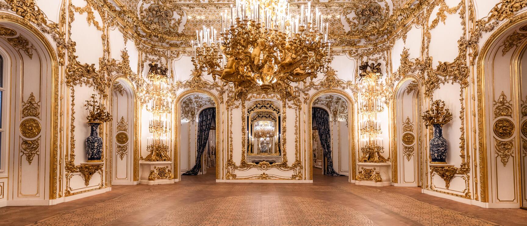 Baroque banquet hall with golden chandelier, white stucco walls and parquet flooring in Vienna's Palais Liechtenstein.