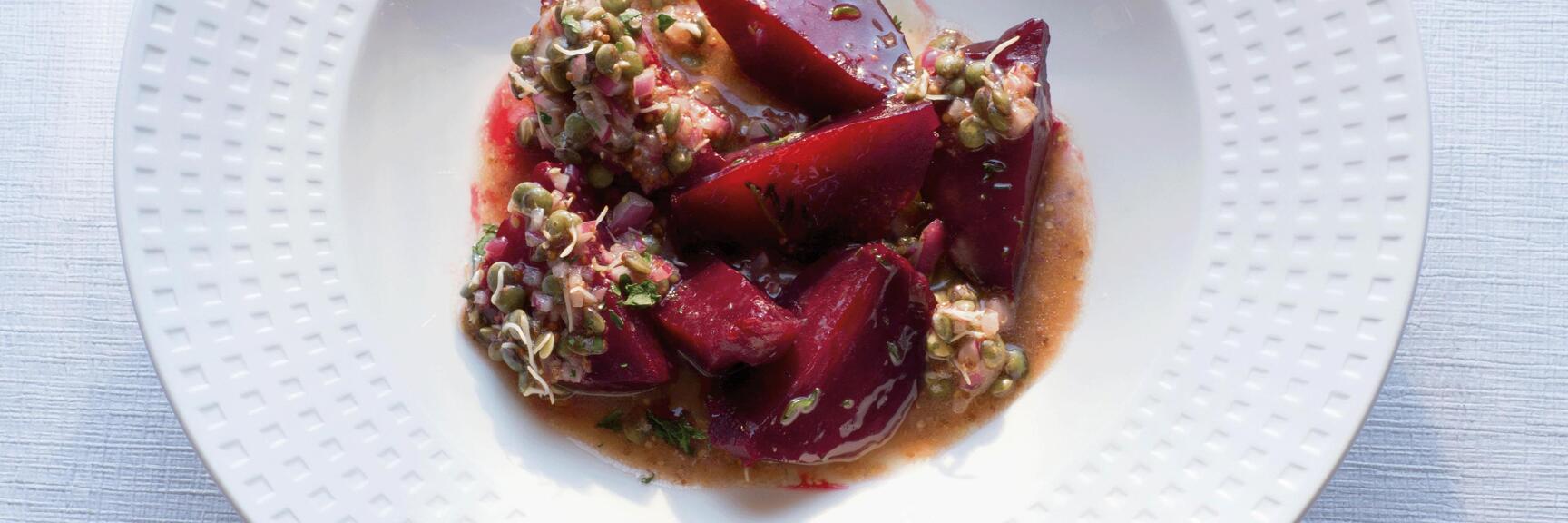 Rote-Bete-Salat mit Linsen und Kräutern in weißem Teller auf hellem Tischtuch.