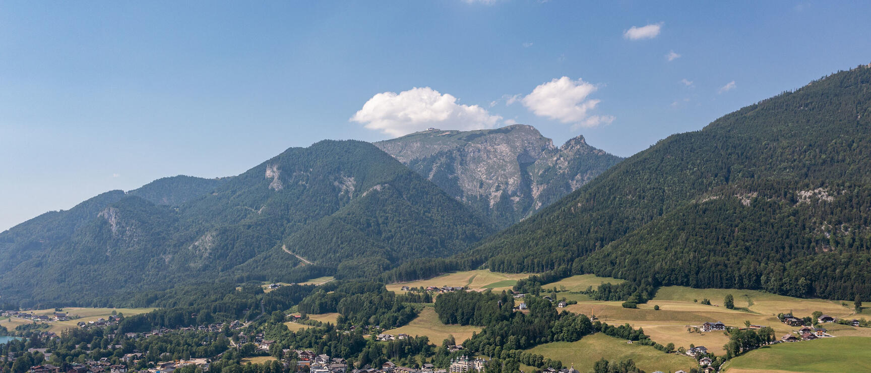 Aerial view of St. Wolfgang am Wolfgangsee with church, village centre and forested mountains in the background.