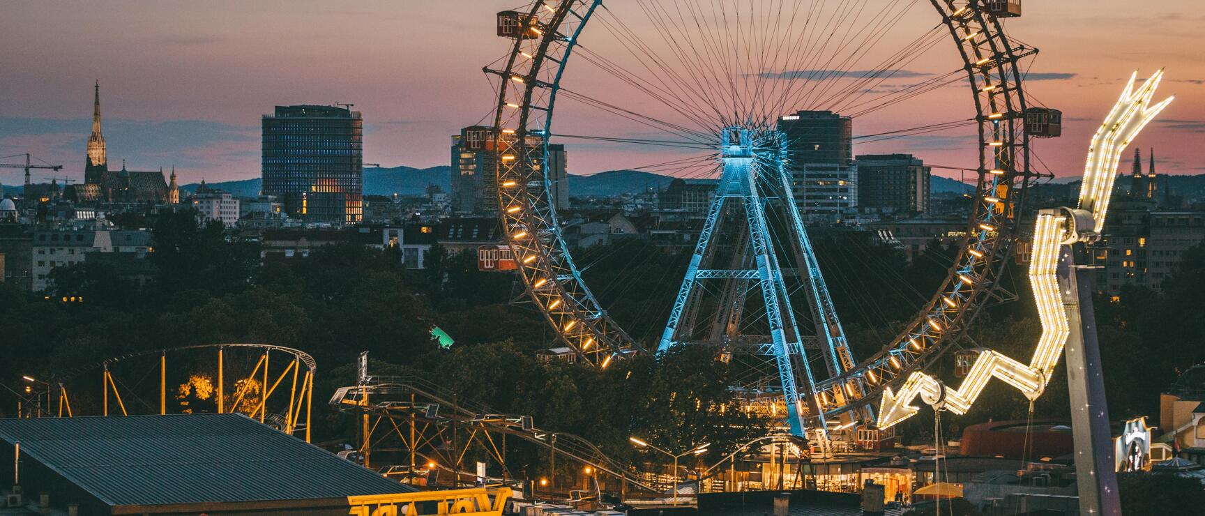 Vienna Giant Ferris Wheel in the Prater at dusk, illuminated, city skyline with church in the background.
