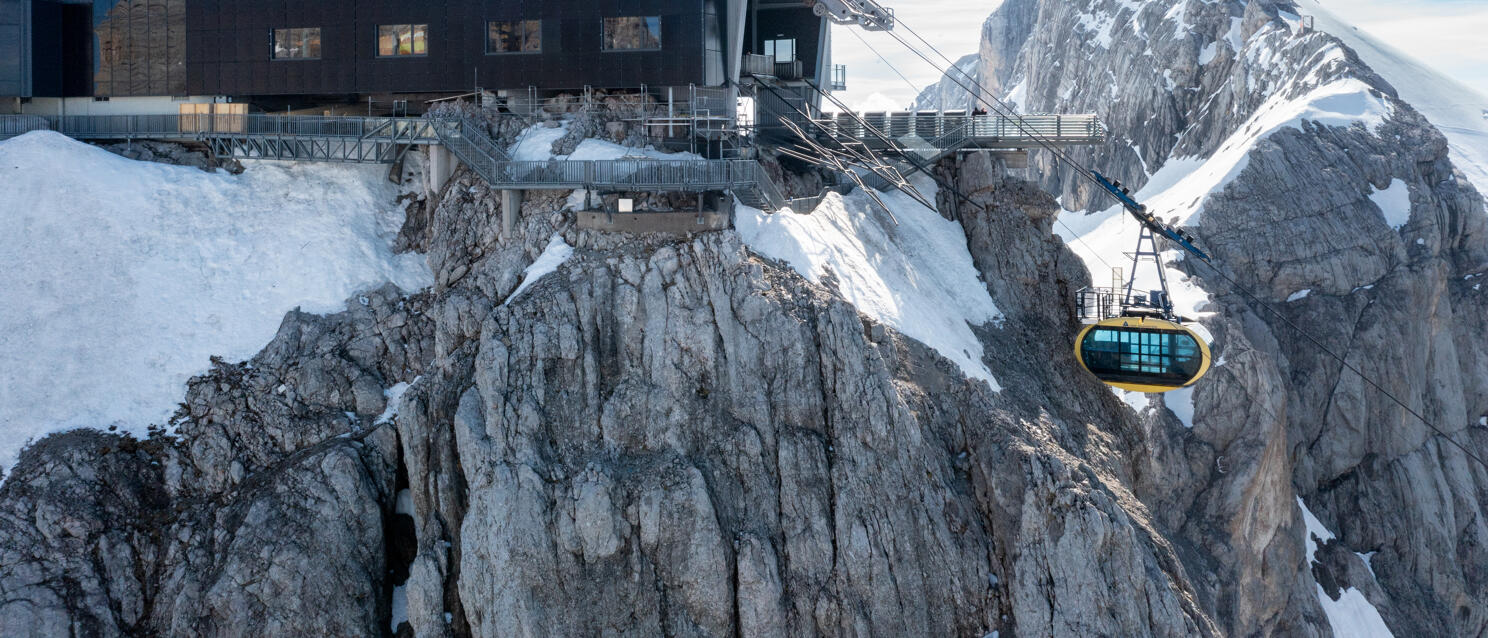 Mountain station on snow-covered rocks, yellow cable car cabin, rocky summit in background, Dachstein.