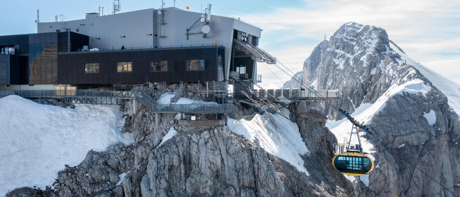 Mountain station on snow-covered rocks, yellow cable car cabin, rocky summit in background, Dachstein.