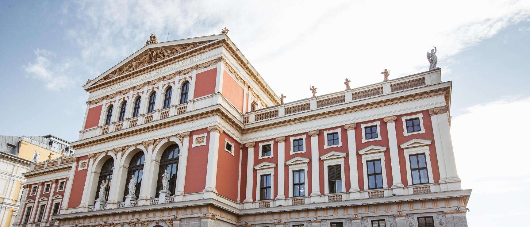 Außenansicht des Wiener Musikvereins mit roter Fassade, weißen Säulen und Skulpturen, Wien.