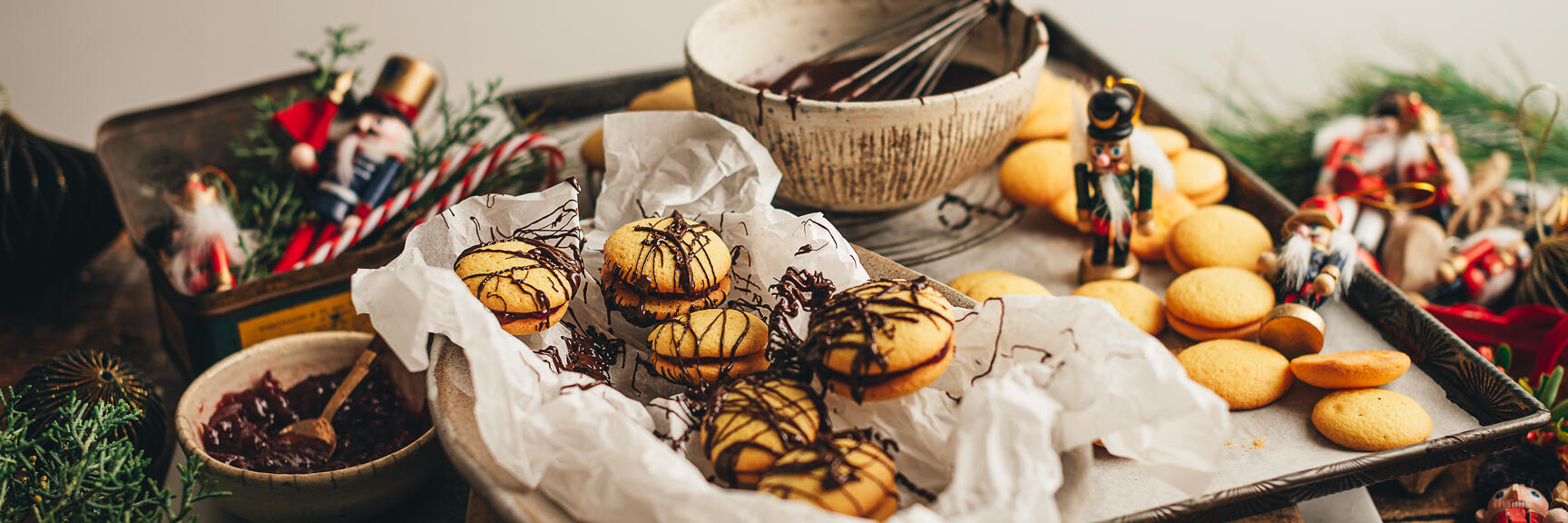 Christmas biscuits with chocolate glaze on baking sheet with bowl, whisk, nutcracker figurines and fir branches