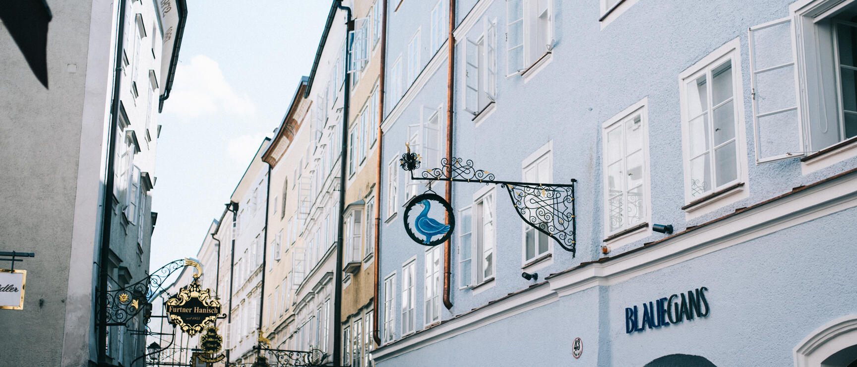 Getreidegasse in Salzburg with wrought iron guild signs, facade of Hotel Blaue Gans, pedestrians.