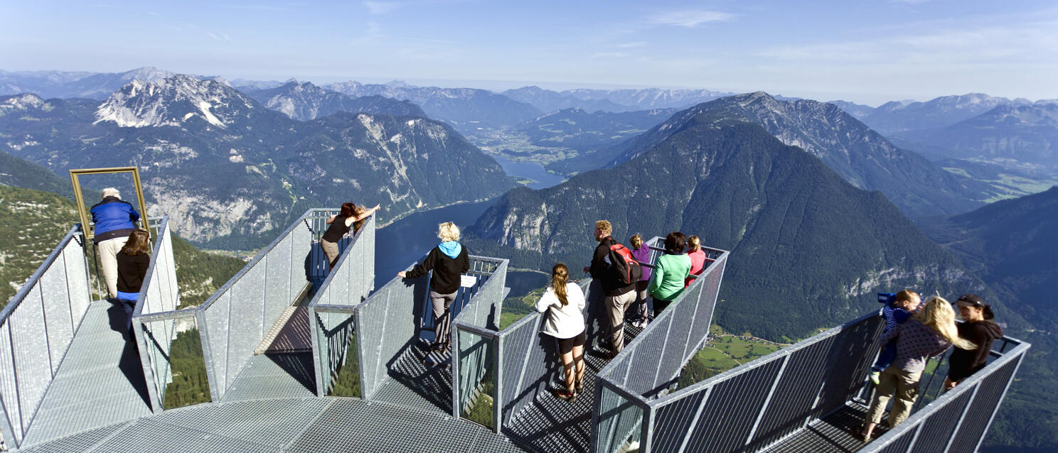Several people on the Five Fingers viewing platform at Dachstein with Hallstatt Lake and mountain panorama in the background.