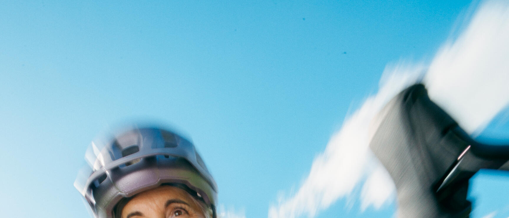 Woman wearing a helmet on a bicycle, close-up of the handlebars, green meadows and blue sky in the background.
