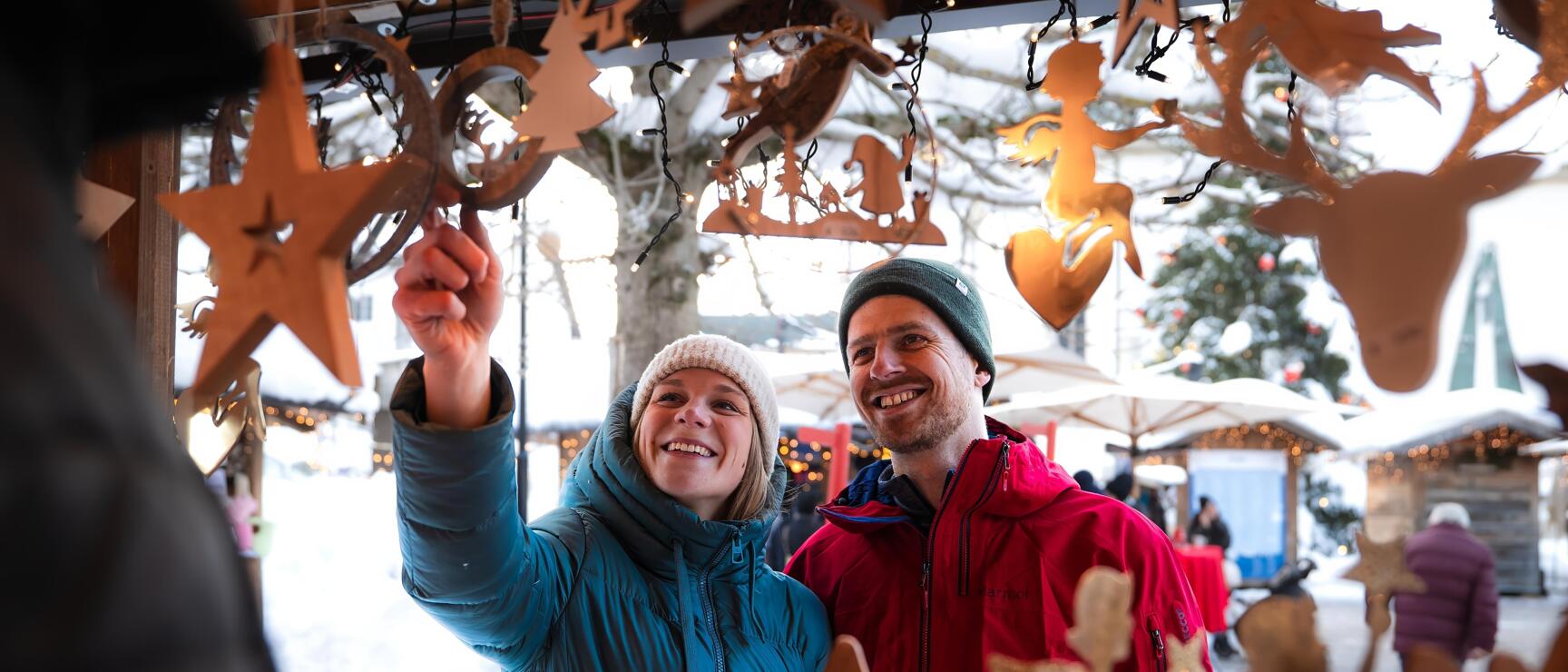 Two people at a wooden ornament stand at a festive Christmas market in winter.
