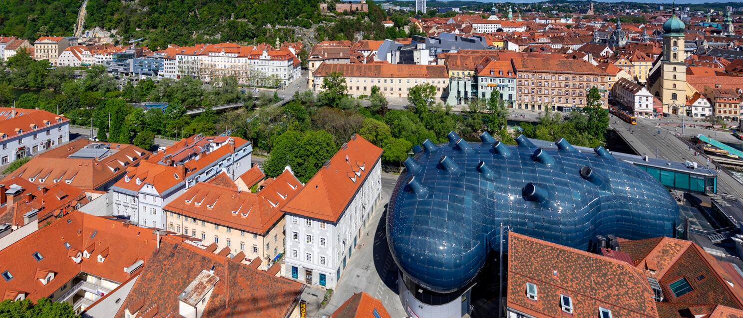 Aerial view of Graz with Kunsthaus, Schlossberg and Clock Tower, red tile roofs of the old town.