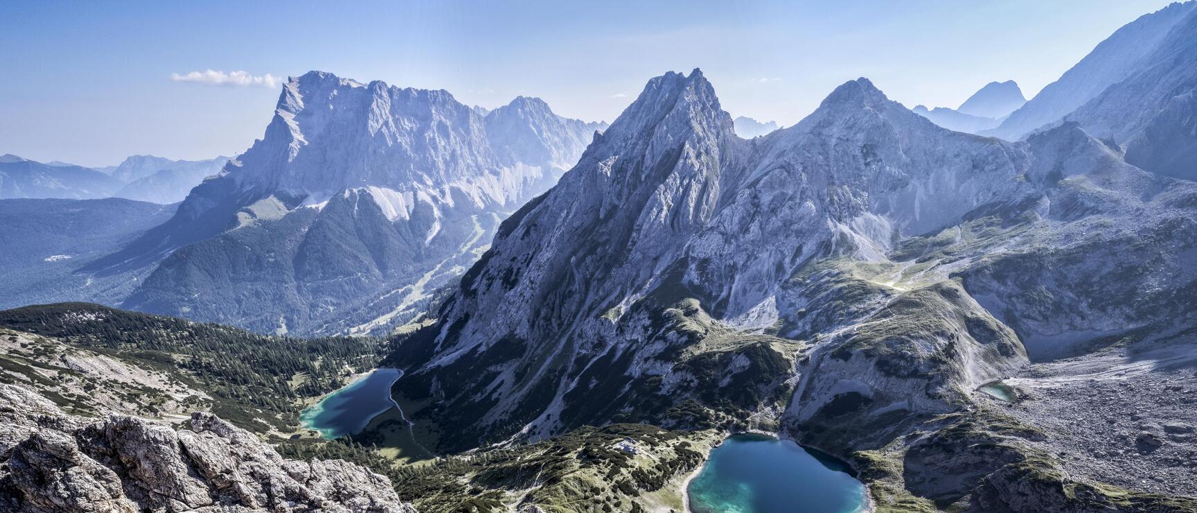 A view from the cliffs of two turquoise-blue mountain lakes, the Seebensee and Drachensee, with the Zugspitze massif in the background.
