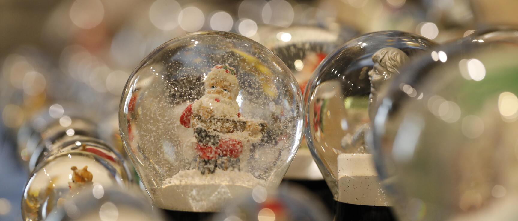 Close-up of several snow globes, one in focus featuring a Santa Claus figure with white snow