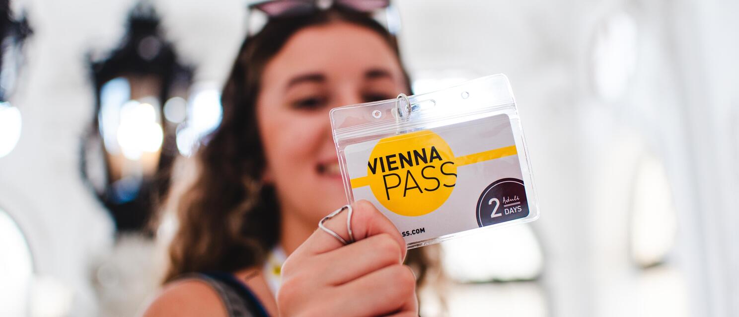 Woman holding Vienna Pass (2 Days, Adults) towards camera, bright background.