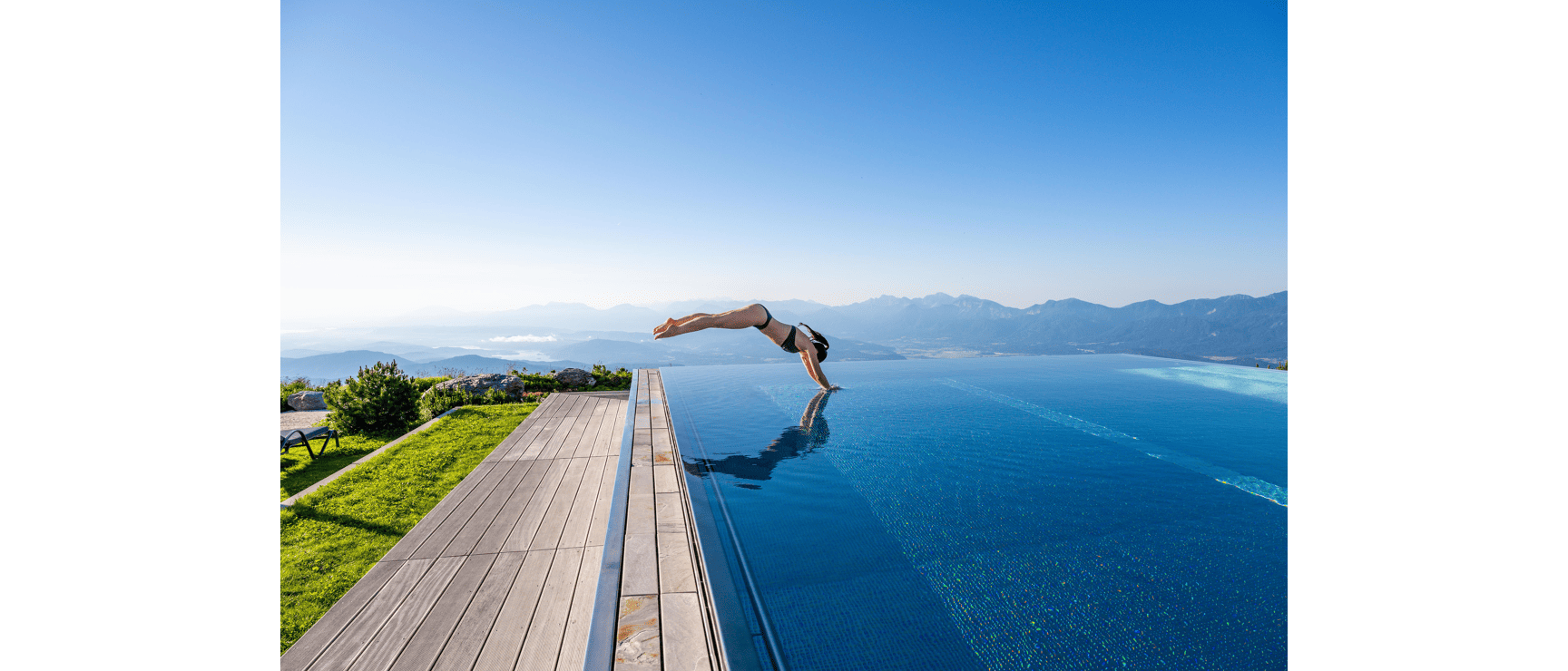 Person diving headfirst into an infinity pool with views of a lake and mountain range in the background.