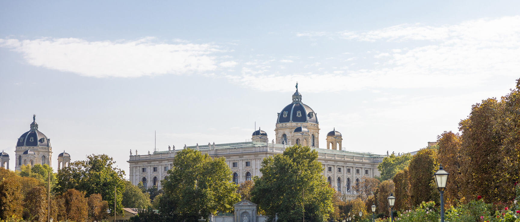 View from Volksgarten to Kunsthistorisches Museum Vienna, park path with roses and benches, people sitting