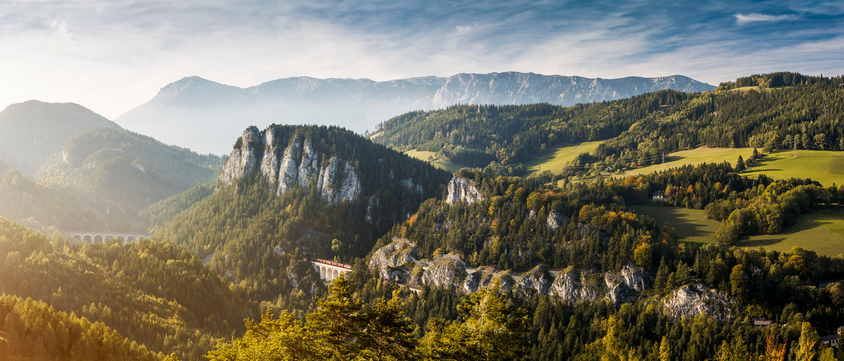 Panoramic view of Semmering area with viaduct, train, rocky cliffs, forests and mountain range in background
