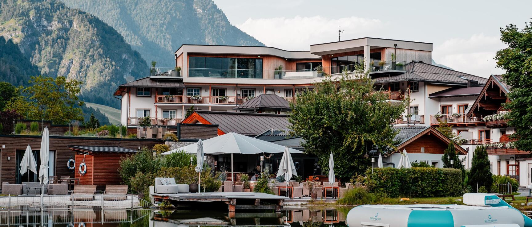 Hotel resort with terrace and umbrellas on a peaceful lake with inflatable raft and mountain backdrop.
