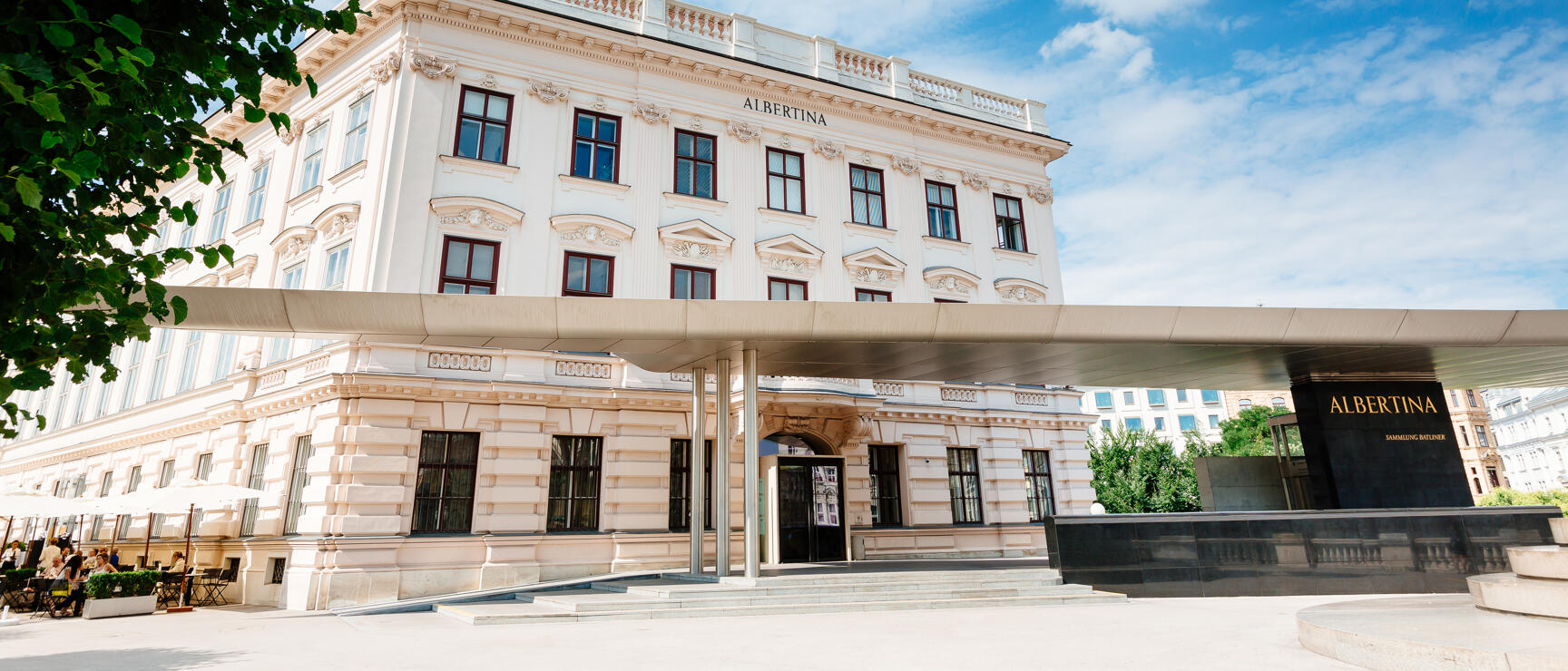 Exterior view of Albertina Modern in Vienna, light Baroque building with modern canopy, blue sky.