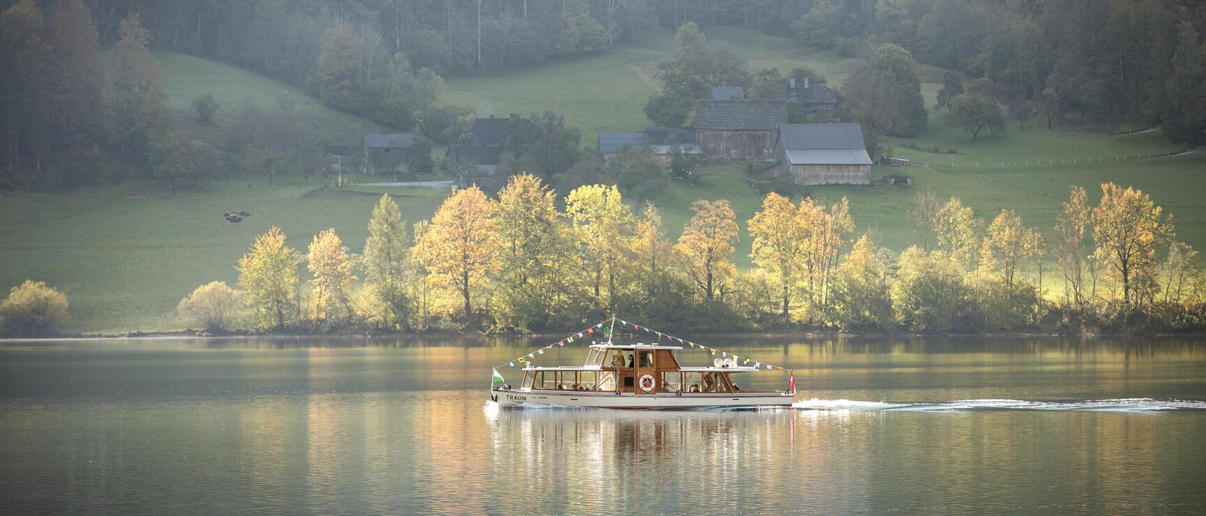 Passenger ship 'Traun' on a lake with autumn trees and farmhouses on the shore in the background.