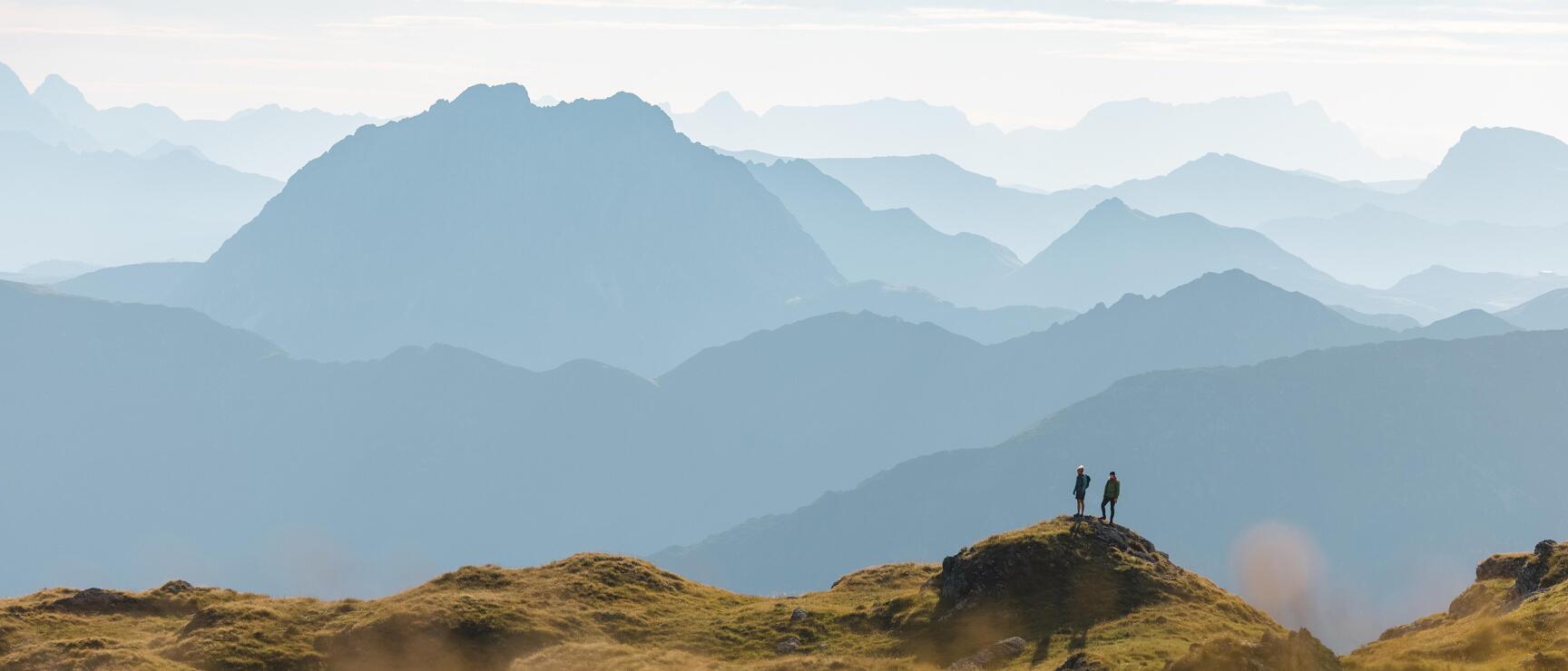 Two people on a rock with layered mountain silhouettes in mist behind them.