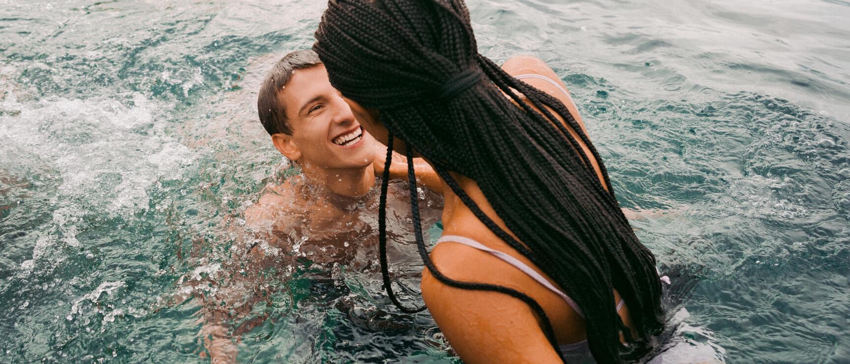 Two people swimming and laughing in clear turquoise water.