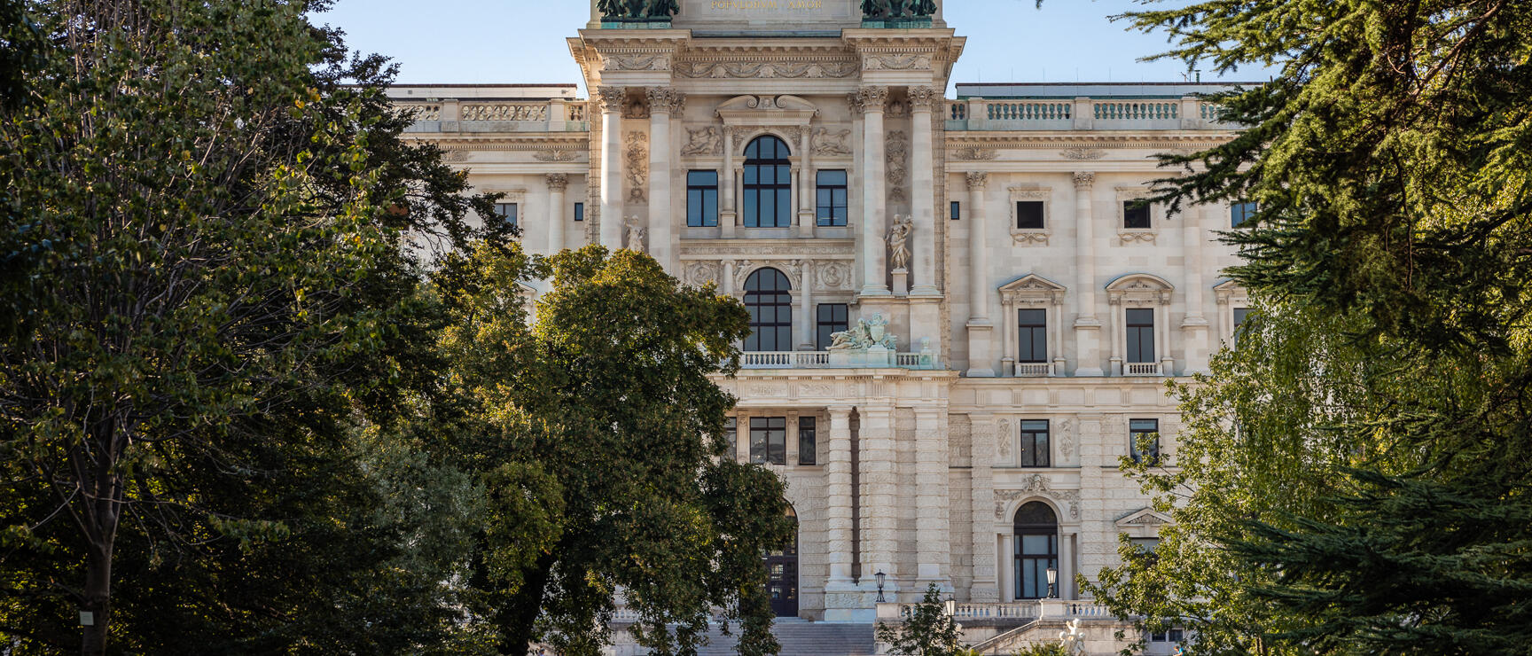 Neue Burg of the Vienna Hofburg, façade with sculptures and golden eagle, framed by trees.
