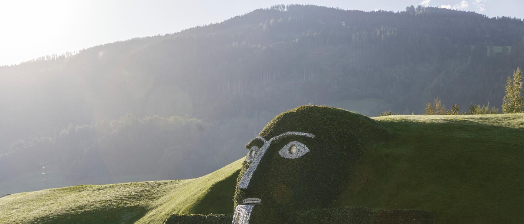 Giant head sculpture with waterfall at Swarovski Crystal Worlds in Wattens, pond and mountain backdrop.