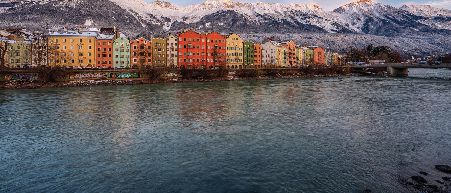 Colourful row of houses on the Inn in Innsbruck, snow-capped mountains in the winter background.