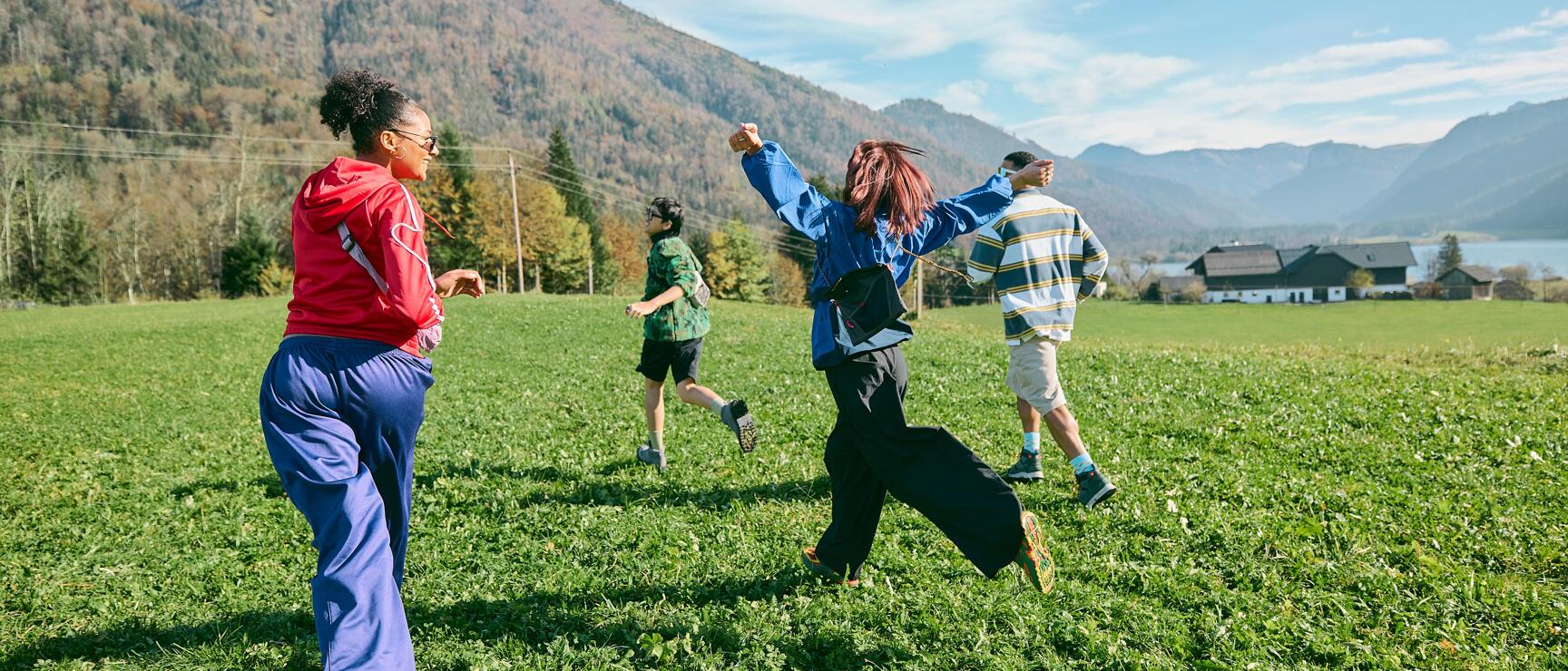 Four people walking across a green meadow with mountain panorama and lake in the background on a sunny autumn day.