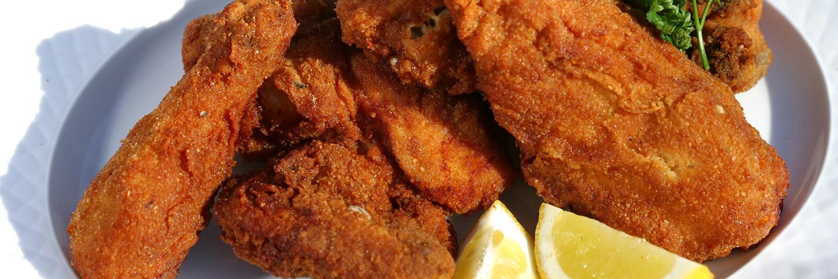 Fried schnitzel on white plate, garnished with lemon wedges and fresh parsley.