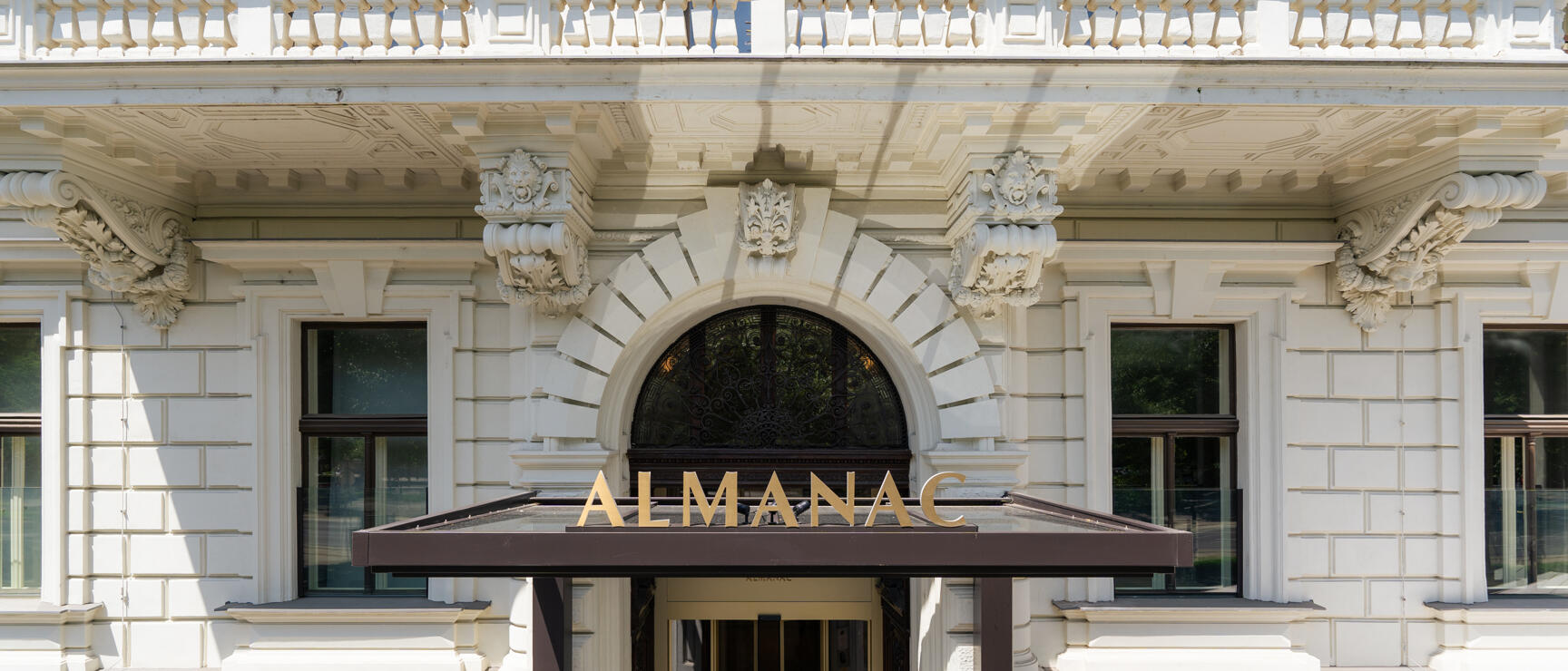 Entrance of Hotel Almanac Vienna, Gründerzeit façade with rounded arch, canopy with golden lettering.