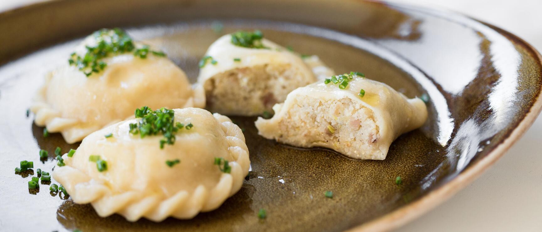 Four filled dumplings with chives on an oval ceramic plate with sauce.