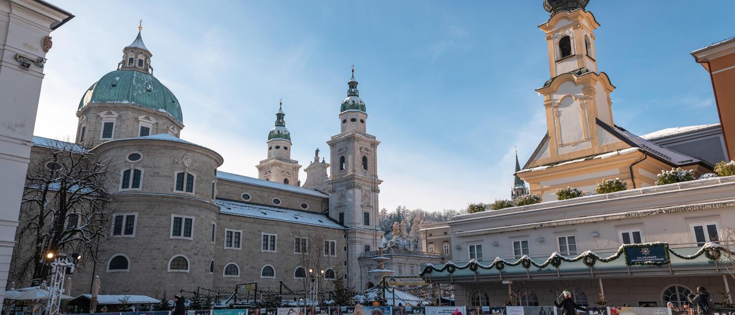 Ice skating rink in front of Salzburg Cathedral in winter with people ice skating and blue sky.