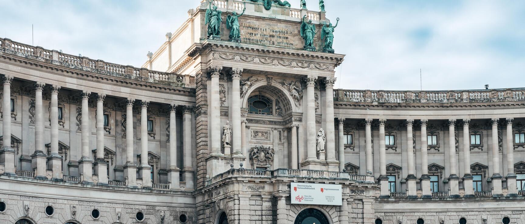 Neue Burg of Vienna Hofburg with bronze statues, golden eagle and national library signage.