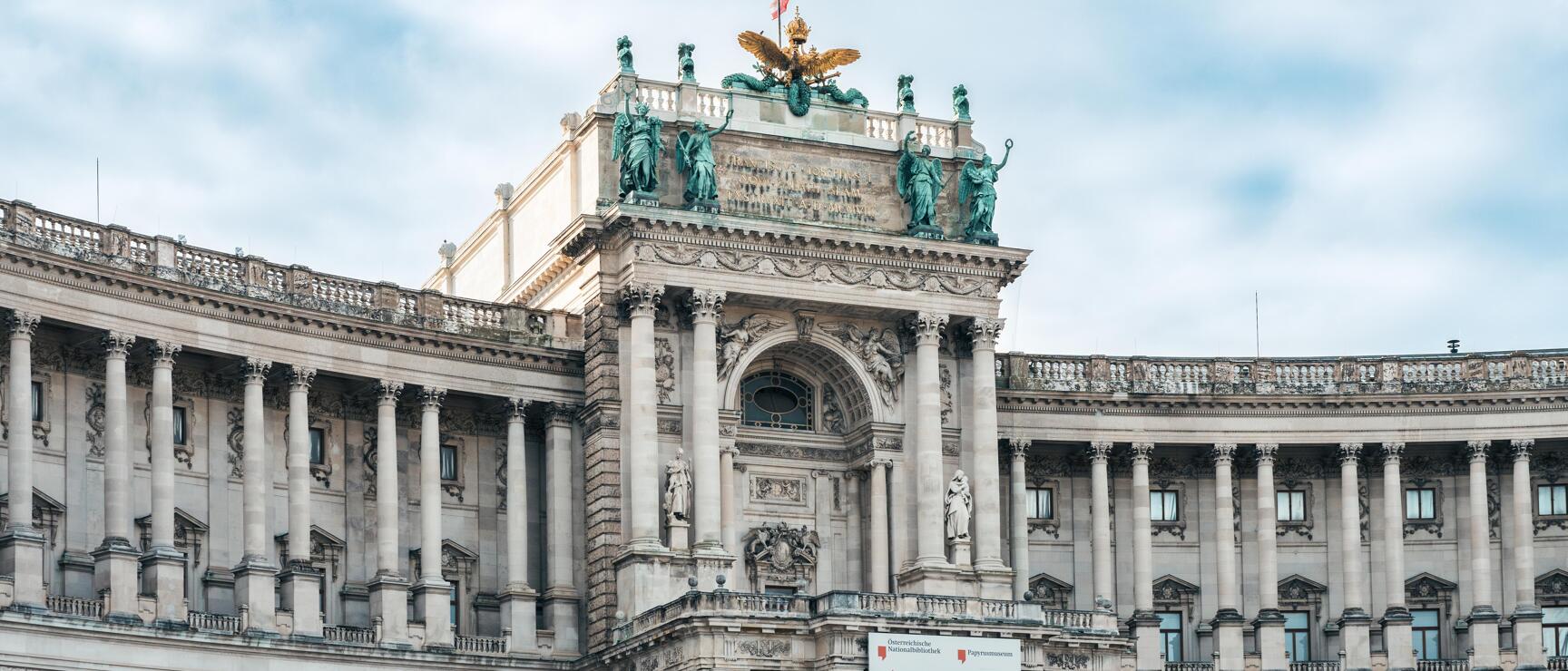 Neue Burg of Vienna Hofburg with bronze statues, golden eagle and national library signage.