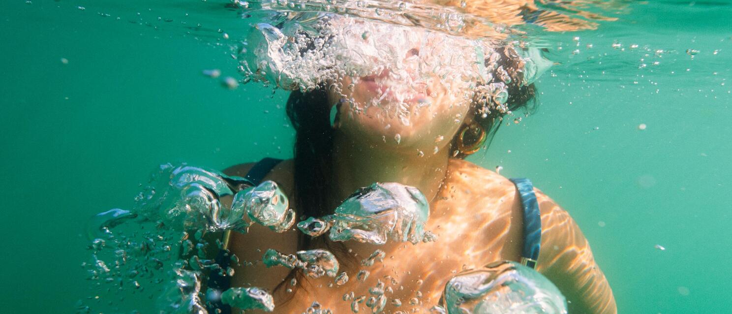 Woman in blue swimsuit diving underwater, bubbles rising, green water.