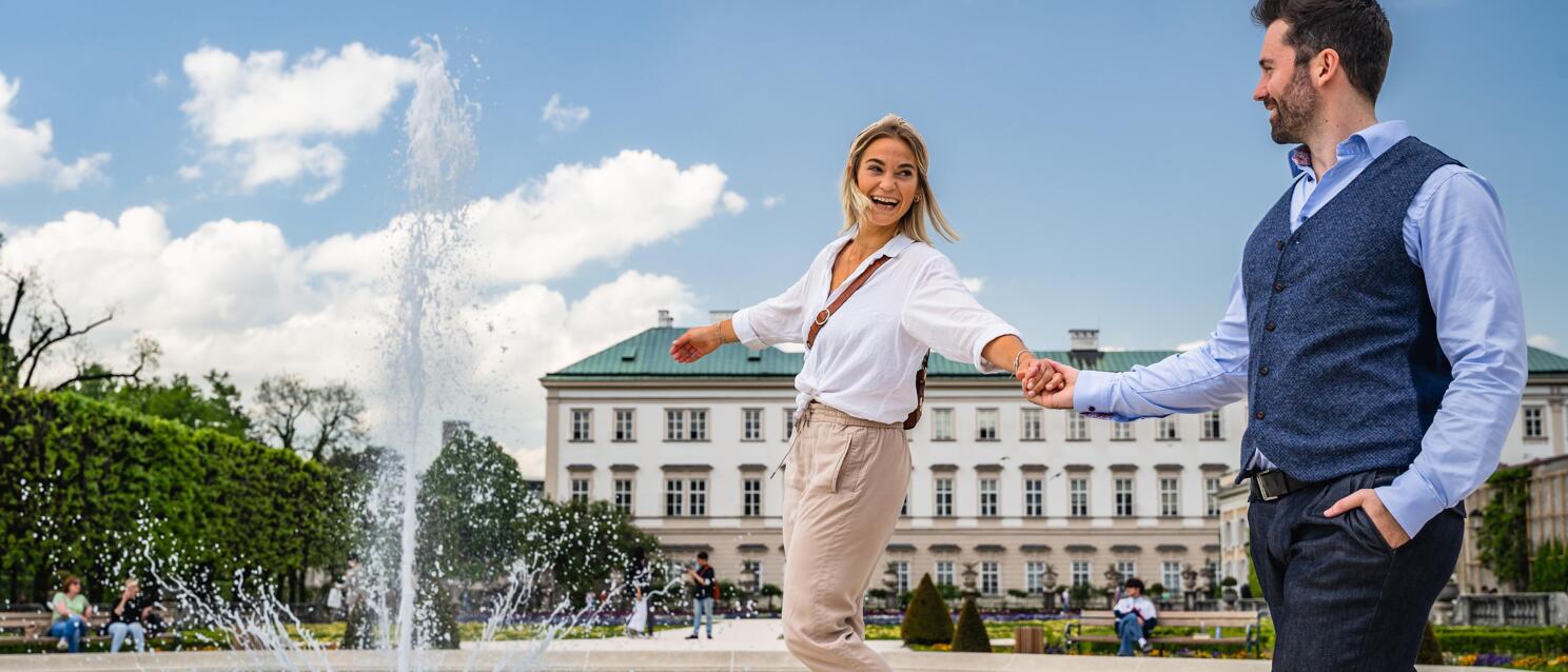 Couple holding hands at fountain in Mirabell Garden, Mirabell Palace in background, Salzburg.