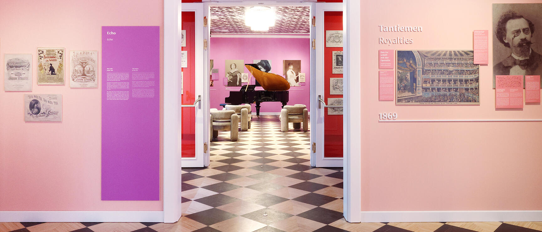 Museum room with pink walls, checkered floor, grand piano in the background and exhibition panels about Johann Strauss.
