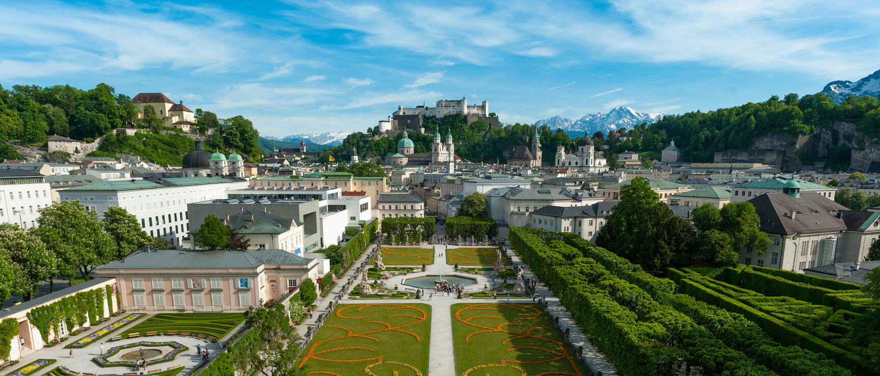 Mirabellgarten Salzburg mit Blumenbeeten, Brunnen, Festung Hohensalzburg und Alpen im Hintergrund.