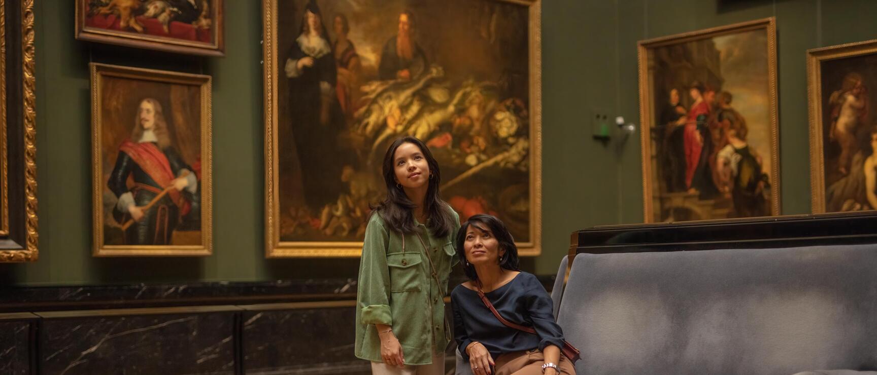Zwei Frauen betrachten Gemälde in einem Museumssaal mit grünen Wänden und Parkettboden, Wien.