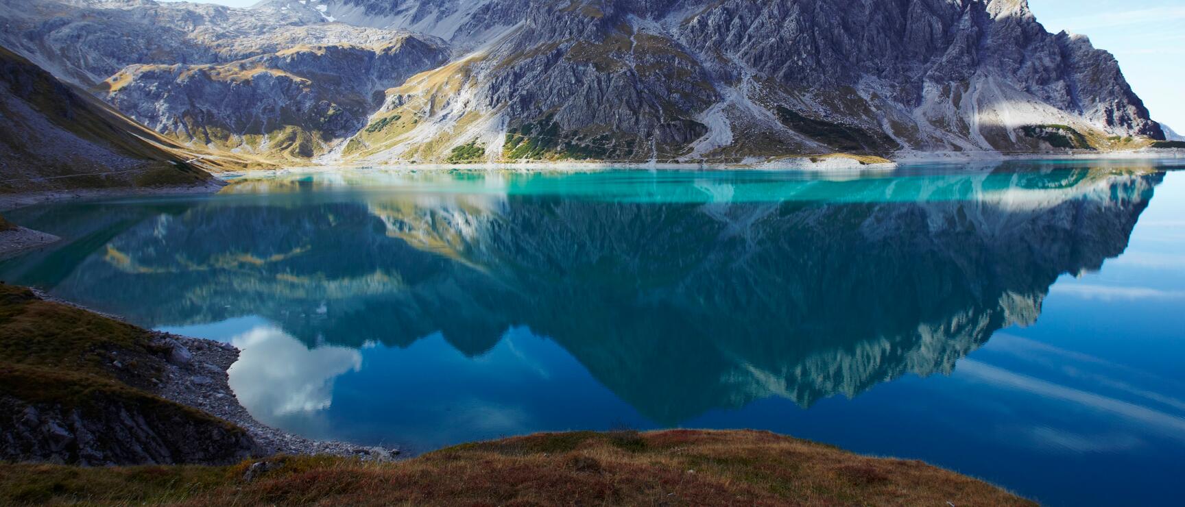 Turquoise blue mountain lake with reflection of rocky peaks, Lünersee, Vorarlberg.