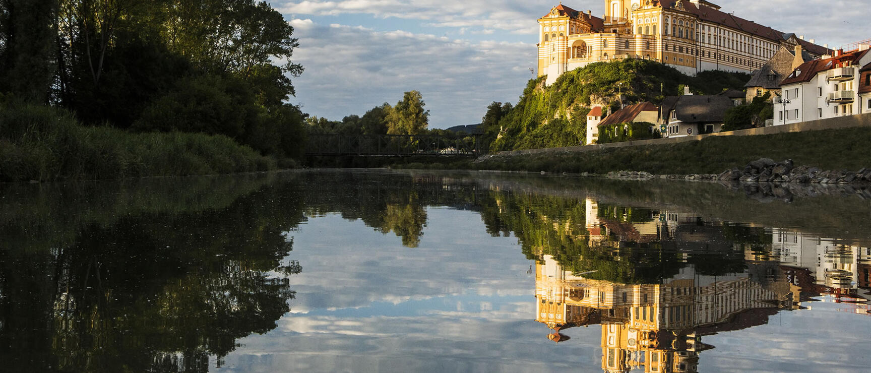 Melk Abbey perched on a rock above the Danube, Baroque façade reflected in calm water.