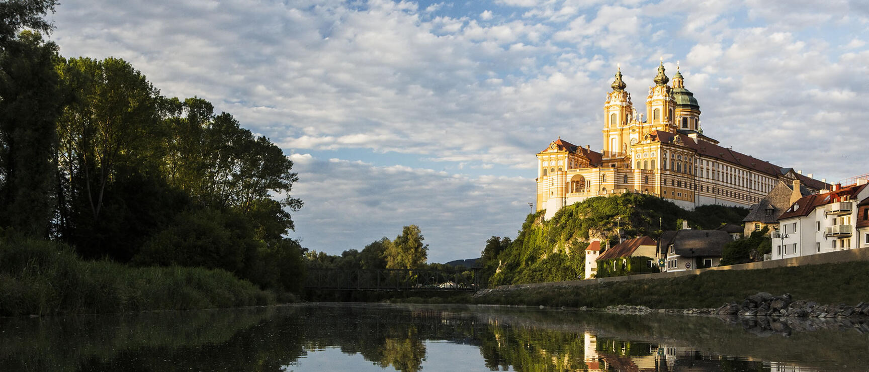 Melk Abbey perched on a rock above the Danube, Baroque façade reflected in calm water.