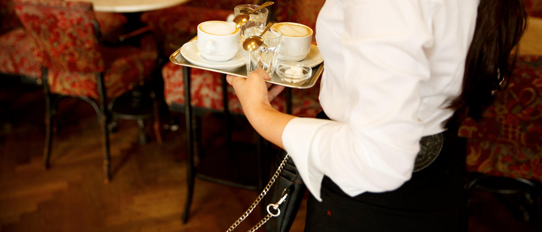 Waitress carries tray with two cappuccinos and glasses of water in a Viennese coffeehouse.