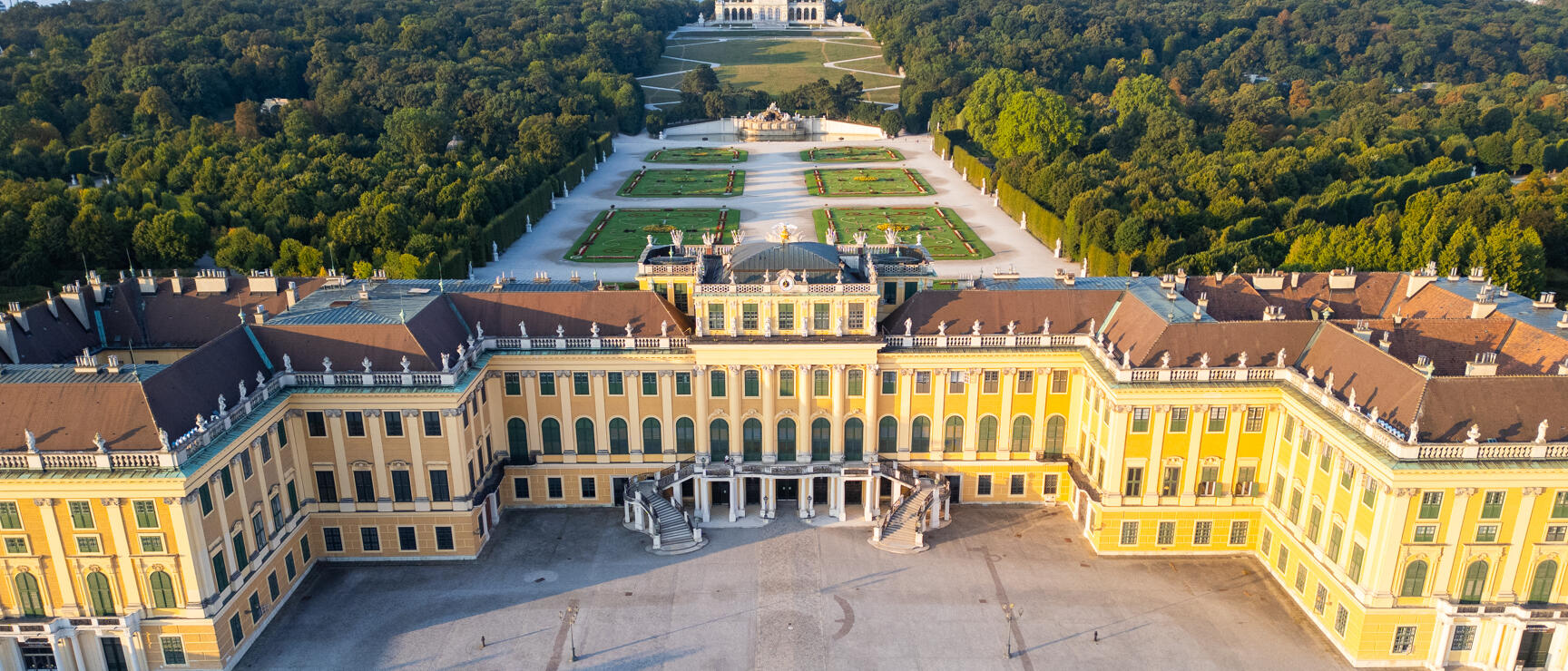 Aerial view of Schönbrunn Palace, Vienna: yellow Baroque facade, courtyard of honour, park grounds with Gloriette in the background.