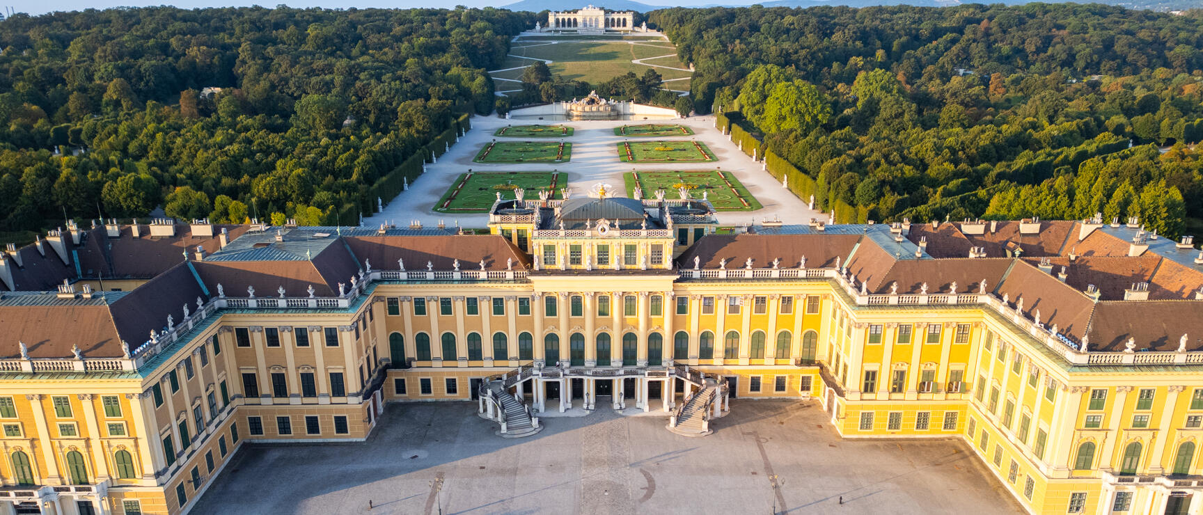 Luftaufnahme Schloss Schönbrunn, Wien: gelbe Barockfassade, Ehrenhof, Parkanlagen mit Gloriette im Hintergrund.